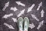 Shot of feet in sneakers with white arrows pointing in all different directions on the ground around them.