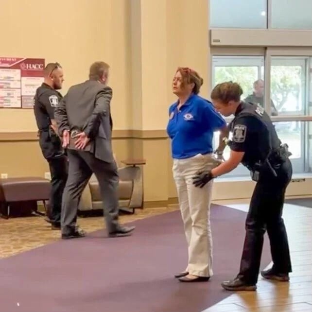 Police place two people in handcuffs in community college hallway.