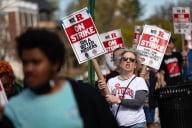 Protesters march, holding signs saying, "We R On Strike for a Better Rutgers."