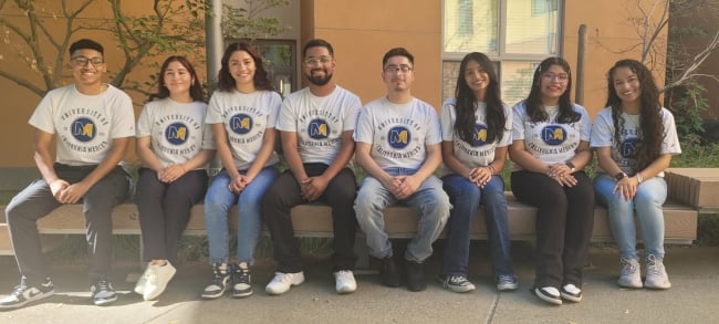 Fiat Lux scholars at UC Merced sit on a bench in a line.