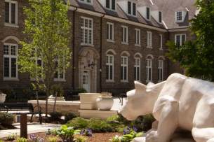 A photograph of a statue of the Penn State Nittany Lion mascot looking toward a building on campus.