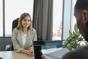 A job applicant smiles across the table at a hiring manager, who holds her résumé.